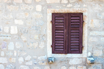 Authentic house with a stone wall, with beautiful old open windows and with green shutters, and with vases on the window.