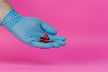 hand with latex gloves carrying red pills on a pink background