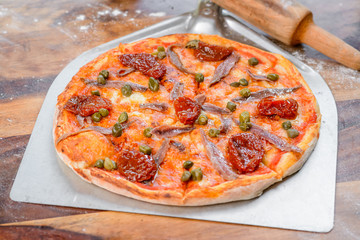 Anchovies pizza on the table with wood roller