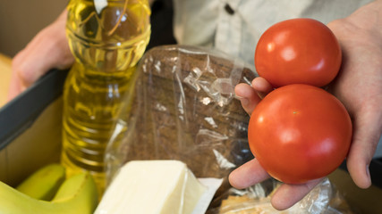 A man puts tomatoes in a donation box. Donations to the needy and the starving during coronavirus. Oil, bread, cucumbers, bananas, tomatoes, cheese.