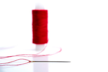 needle with red thread on the background of a spool of thread