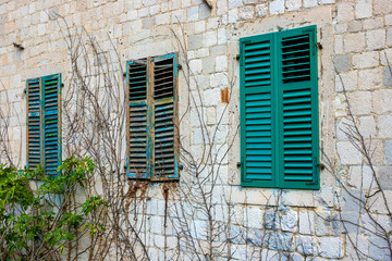 Fototapeta na wymiar Authentic house with a stone wall, with beautiful old open windows and with green shutters, and with vases on the window.