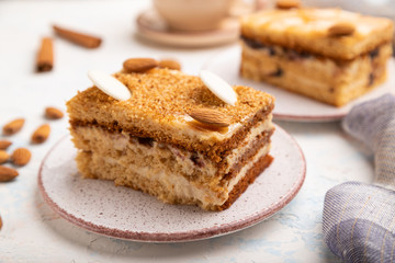 Honey cake with milk cream, caramel, almonds and a cup of coffee on a white concrete background. Side view, selective focus.
