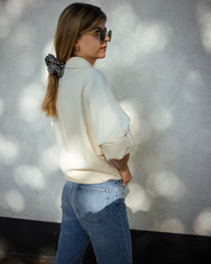 Young woman is posing in front of a wall, casual chic.