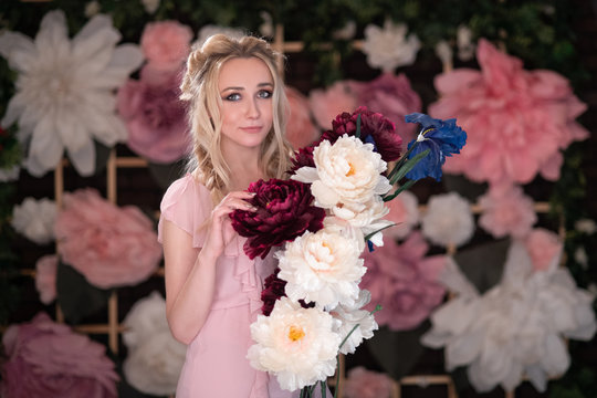 a blonde girl with 2 pigtails on the background of a flower wall with a sprig of large artificial flowers