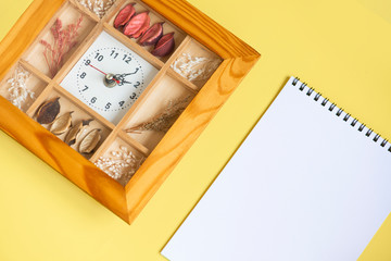 Wooden wall clock and paper notebook on a yellow background. Empty space for text.