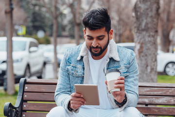 Fototapeta premium Bearded Indian man sitting on a bench and using his tablet.