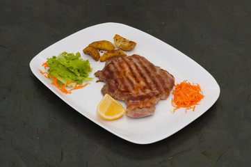 Juicy grilled meat steak with lemon, carrots, lettuce and potatoes.