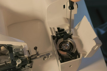 Seamstress woman is repairing mechanism of sewing machine in workshop, closeup hands view. Maintenance and repair of home appliances. Repairing using screwdriver screwing bolt.