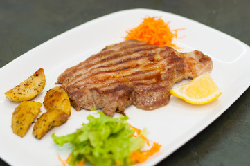 Juicy and delicious grilled meat steak with lemon, carrots, lettuce and potatoes.