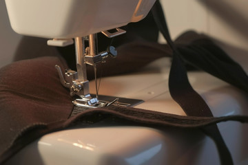 Seamstress is working sewing clothes in sewing machine, hands closeup. Process of sewing in atelier or workshop. Tailoring and repair of clothing, bra, top, brassiere. Self-employed employee.