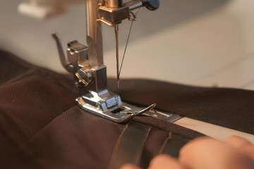 Seamstress is working sewing clothes in sewing machine, hands closeup. Process of sewing in atelier or workshop. Tailoring and repair of clothing, bra, top, brassiere. Self-employed employee.