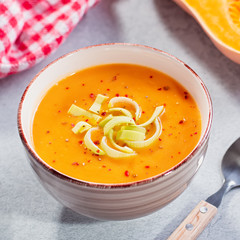 Hot pumpkin or carrot cream soup with spices on concrete background. Closeup of autumn spicy soup, healthy eating, top view