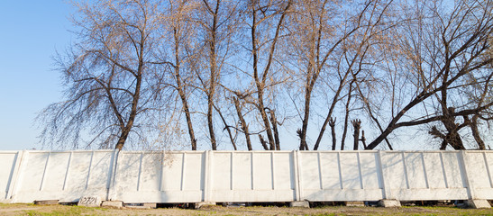 Fototapeta premium White concrete slabs - a municipal fence enclosing a building site against the sky and trees. City building along restricted facilities.