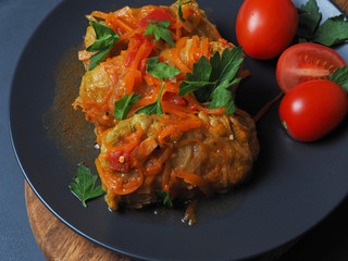 Cabbage rolls with meat, rice and vegetables. Stuffed Peking cabbage leaves with meat, in tomato sauce, on a black plate with tomatoes and herbs.