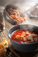 Borsch is poured into a bowl from a ladle from which steam, a traditional Ukrainian vegetable soup made from beets, carrots, tomatoes, potatoes, cabbage, herbs and garlic, close-up, shallow depth of