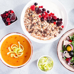 Carrot cream soup, Greek salad, granola bowl with yogurt on concrete table top with copy space. Assortment of dishes for diet, suitable for volumetrics diet and other nutrition strategies, top view