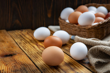 Farm eggs white and brown lie on a wooden table and in a basket, close-up, low light, selective focus, shallow depth of field. Organic food concept