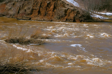 Waterfall on river near mountain at spring with naked bushes, flood, high water. Abandoned hydroelectric power station on river waterfall with streaming current. HPP object.