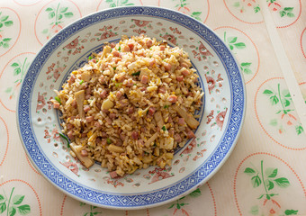 A plate of fried rice with ham and mushroom served on a table in a restaurant