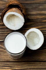 Fototapeta na wymiar Coconut vegan milk in a glass and coconut broken in half on a dark wooden background