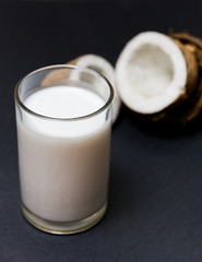 Coconut vegan milk in a glass and coconut broken in half on a dark background