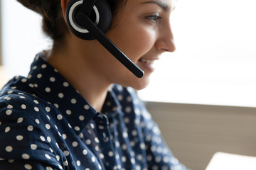 Close up head shot side view pleasant pretty smiling indian woman wearing headset with microphone,...