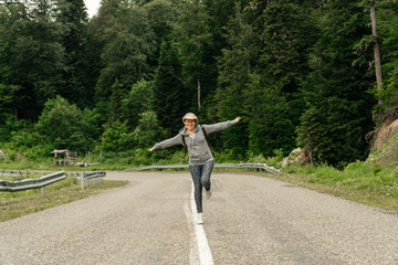 Attractive young woman walks along the line of the road with hands raised enjoying nature.