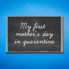 Mother's Day concept: 3D rendered blackboard with white chalk written MY FIRST MOTHER'S DAY IN QUARANTINE in hand writing letters. Board hanging on blue wall