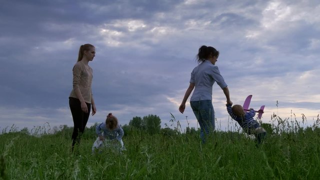 Family Playing with Toy Airplanes in Grass Field. Happy Mother and Children. Spring Evening Rural Nature