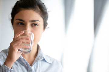Head shot face close up healthy young indian girl drinking pure water. Pretty millennial mixed race...