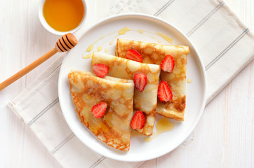 Homemade crepes with strawberry slices and honey