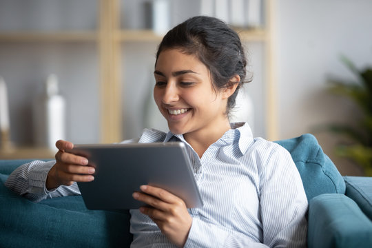 Head Shot Close Up Cheerful Young Indian Girl Holding Computer Tablet, Looking At Screen. Smiling Millennial Woman Watching Funny Video, Comedian Movie, Playing Entertaining Online Game At Home.