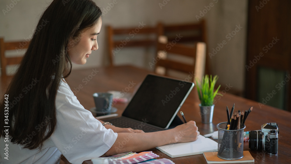 Poster young asian female designer using graphics tablet while working with computer at home.
