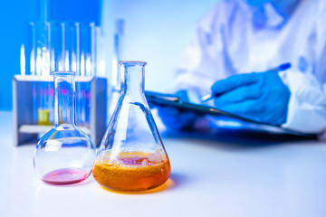Laboratory assistant records the results of the experiment with chemical liquids. The hands of the assistant and flasks of chemical fluids. Quality control. Laboratory analysis of chemical samples.