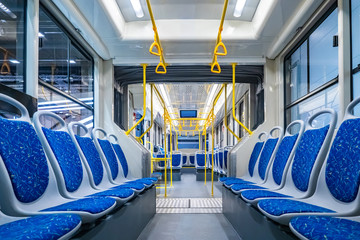 Public transport. Empty interior of the city bus. Rows of blue passenger seats and yellow handrails. The interior is equipped with handrails and hanging handles.