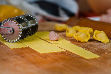 Homemade tortellini with little filling, the pasta cutter and the square sizes of pasta.