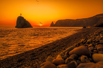 view of the sunset sea and the beach, the volcanic rock is lit by the warm sunset, sand and...