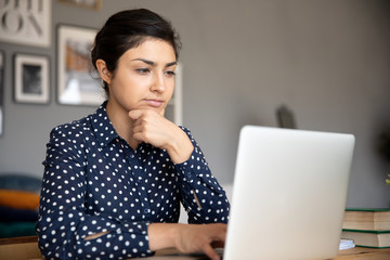 Head shot thoughtful young indian woman looking at computer screen. Focused millennial female...