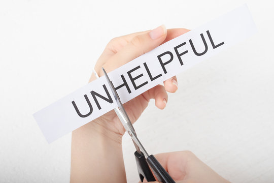 The concept of self-confidence and success. Female hands scissor the word unhelpful