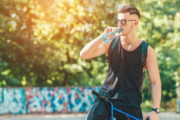 man drink water with bottle sitting on bmx bike on sunshine background