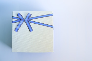 Top view of white gift box or present box package with a blue ribbon and bow on a blue and white background with copy space for your text. Symbol of love and surprise.