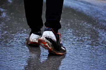 Man feet wearing old and broken sneakers/ broken sneakers walking in the rain