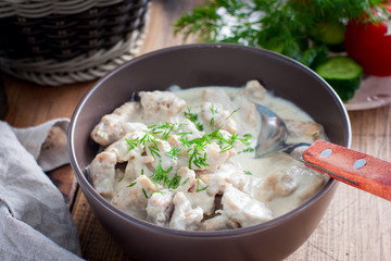 Stewed pork in sour cream in a ceramic bowl on a wooden table, selective focus