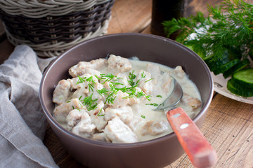 Stewed pork in sour cream in a ceramic bowl on a wooden table, selective focus