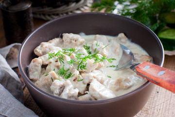 Stewed pork in sour cream in a ceramic bowl on a wooden table, selective focus
