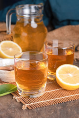 A glass of iced tea with mint and lemon on a wooden table.A glass cup of tea with lemon, mint, and honey on a wooden rustic table.