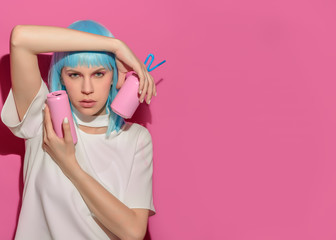 Portrait of young woman with blue hair holds in hands soda bottle on pink background. Pink metal aluminum beverage drink can. Summer boring, tedious party poster. Copy Space