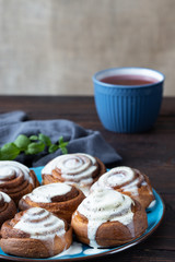 Cinnamon rolls on a plate on a rustic wooden table and a cup of tea. Close view