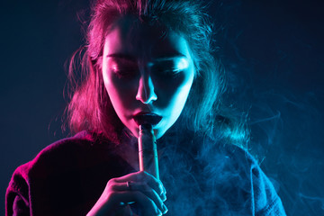 Electronic cigarette. Beautiful girl with a VAPE in neon light. A girl with downcast eyes smokes an...
